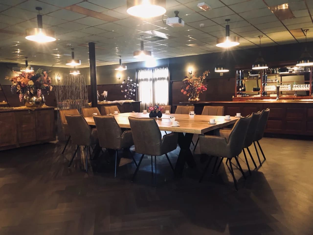 Zaal met een lange tafel, leren stoelen, bloemstukken en een eigen bar aan de zijkant