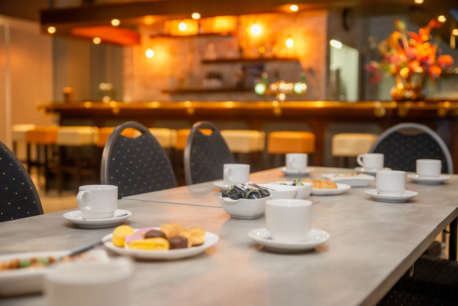 Lange gedekte koffietafel met kopjes en gebak voor de bar in de zaal